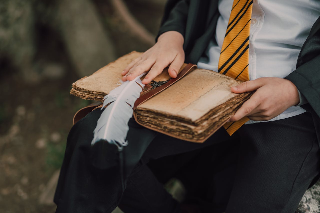 A child in a wizard costume reading an ancient spell book outdoors using a feather quill.